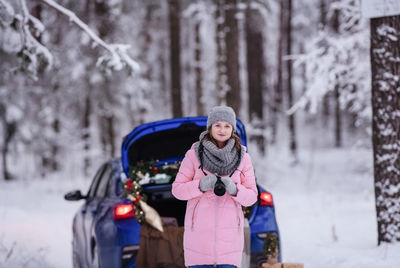 A woman in a winter snow-covered forest in the trunk of a car decorated with christmas decor.