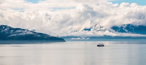 Ship sailing in sea against cloudy sky