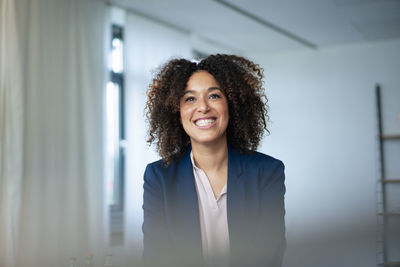 Happy businesswoman with curly hair clenching teeth at workplace