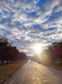 Road amidst trees on field against sky at sunset