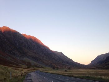 Road leading towards mountains against clear sky