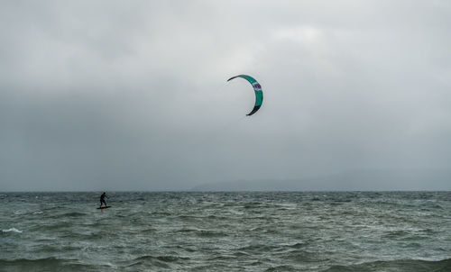 Man kiteboarding in sea against cloudy sky