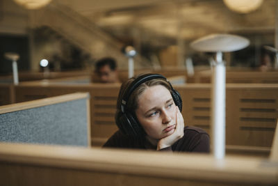 Contemplative young female student with hand on chin in library at university