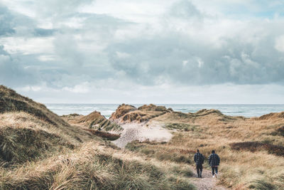 Rear view of people walking on land against sea and sky