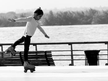 Girl roller skating on footpath against lake