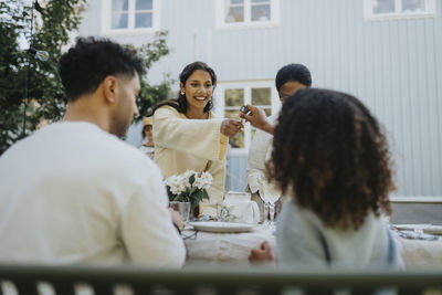 Smiling woman passing spoon to female friend during dinner party in garden