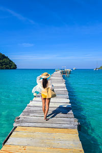 Rear view of woman standing on pier over sea against blue sky