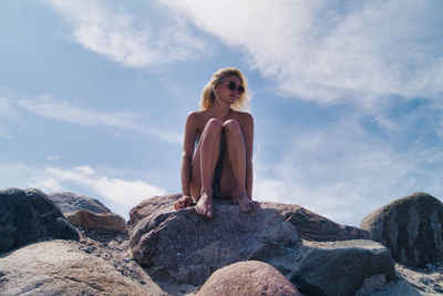 Portrait of woman sitting on rock against sky