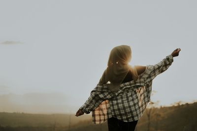 Rear view of woman standing against sky during sunset