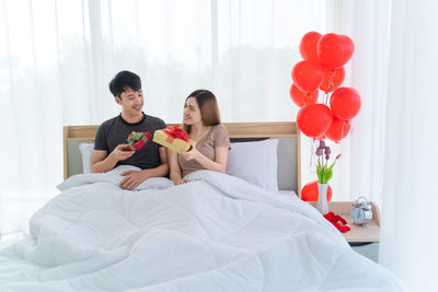 Rear view of couple holding while sitting on bed