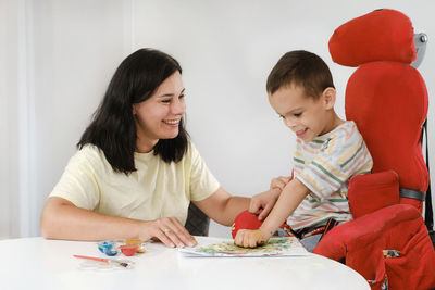 Child with cerebral palsy painting with fingers and hands. happy handicap boy developing fine motor