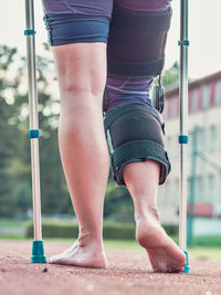 Hurts sports woman walks with knee brace after an injury by medical sticks. tired barefoot woman.