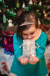Girl holding christmas present against tree