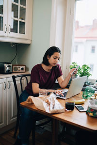 Young woman using phone while sitting on table at home