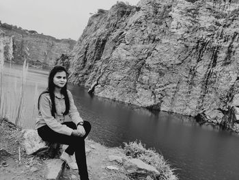 Portrait of young woman sitting on rock by lake