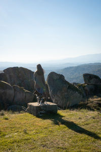 Caucasian young woman with brown dog on top of a boulder stone seeing sortelha landscape