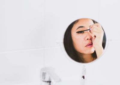 Reflection of woman applying mascara in mirror 