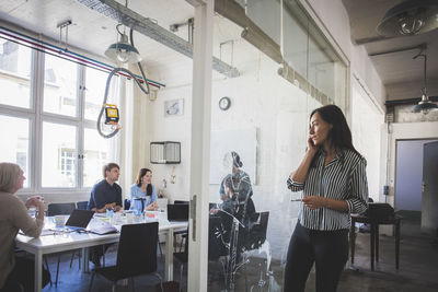 Businesswoman looking at colleagues planning strategy in board room while talking on mobile phone