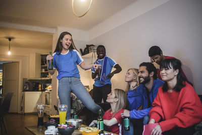 Smiling woman pointing at female while watching sport with friends at home