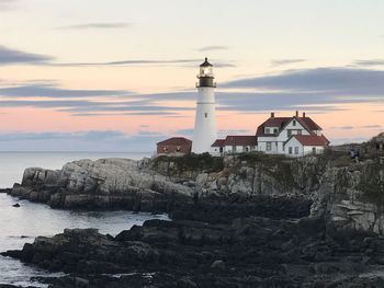 Lighthouse by sea against sky during sunset