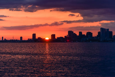 Sea by buildings against sky during sunset