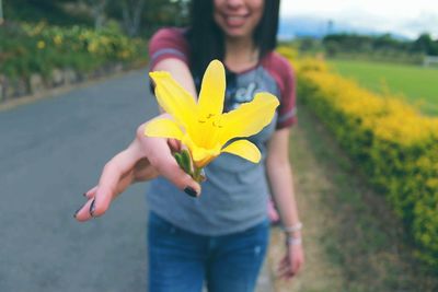 Midsection of smiling woman holding flower while standing on footpath