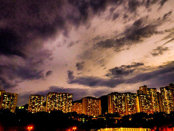 Illuminated buildings in city against dramatic sky at night