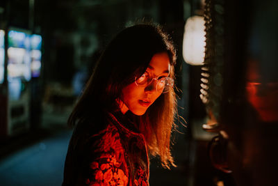 Portrait of smiling young woman standing by illuminated light at night