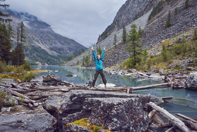 Full length of woman with arms raised standing against mountain