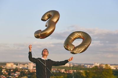 Man with arms raised against sky