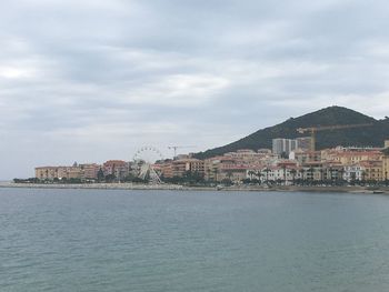 Buildings at waterfront against cloudy sky