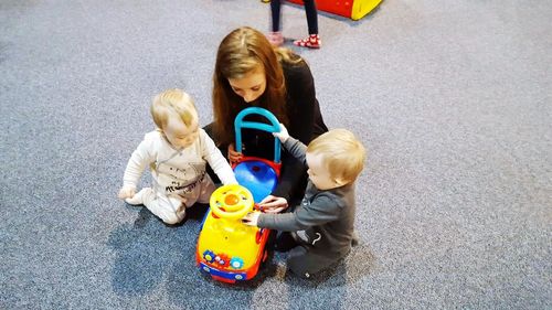 High angle view of mother and twin babies playing with toy car on floor
