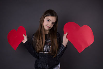 Young woman holding heart shape over black background