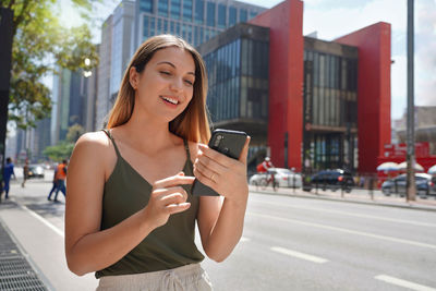 Brazilian girl using mobile phone app for chat on sunny day on paulista avenue in sao paulo, brazil