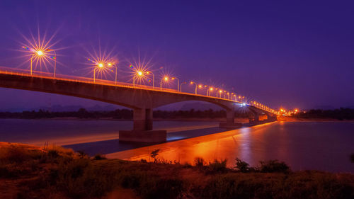 Illuminated bridge over river against sky at night