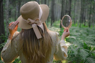 Rear view of woman holding hand mirror standing in forest