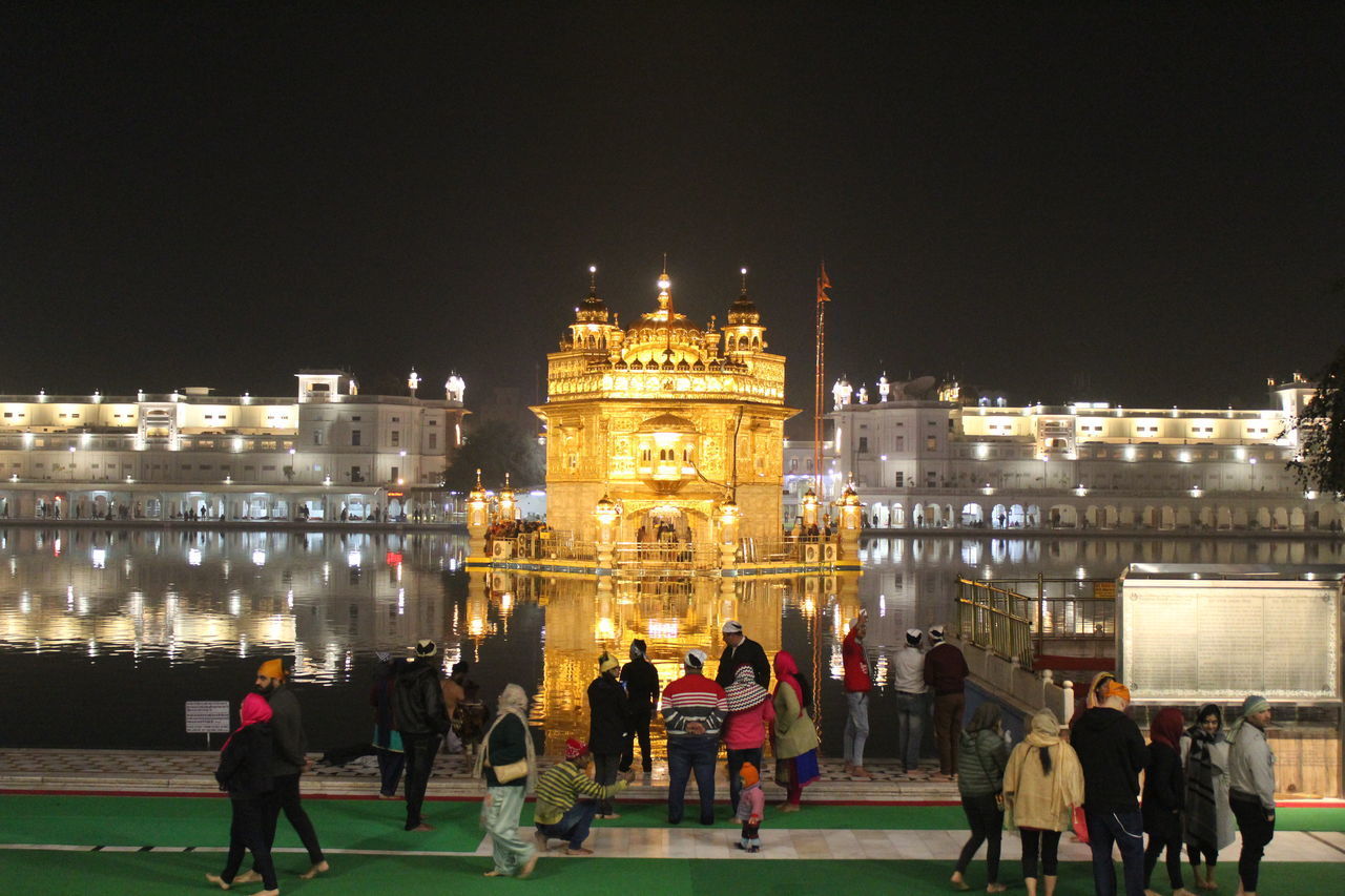 PEOPLE AT ILLUMINATED CITY AGAINST CLEAR SKY