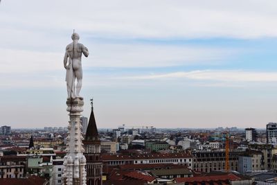 Statue of buildings in city against cloudy sky