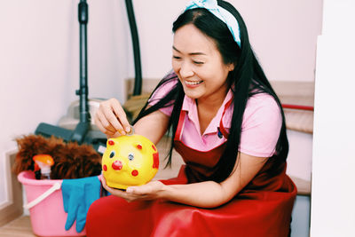 Young woman holding a smiling while sitting against wall