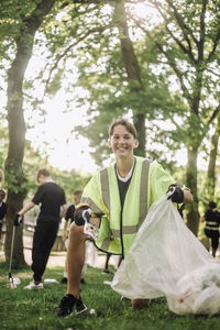 Portrait of smiling teenage boy collecting plastic in garbage bag