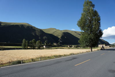 Road by trees and mountains against clear sky