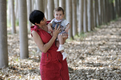 Portrait of grandmother holding granddaughter while standing amidst trees in forest