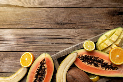Fresh tropical fruits in a wooden delivery box on wooden background. papaya, orange, banana, coconut