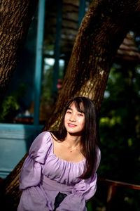 Portrait of smiling woman against tree trunk