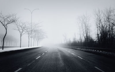 Empty road by bare trees against sky