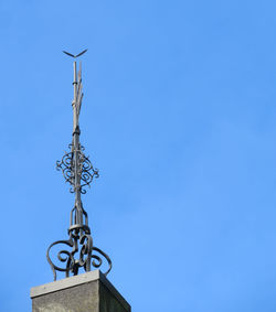 Low angle view of weather vane against blue sky