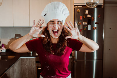 Woman wearing chef hat showing messy hands while standing in kitchen