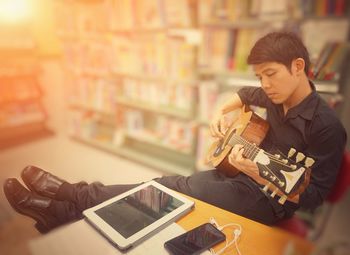 Full length of man playing guitar while sitting in library