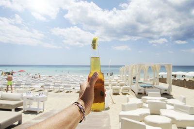 Midsection of woman holding drink at sea against sky