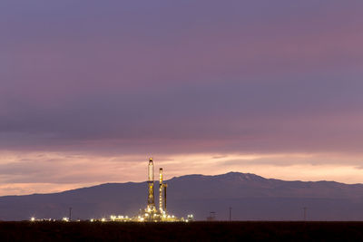 Drilling rig on field against cloudy sky